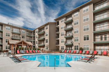 a swimming pool with red chaise lounge chairs in front of an apartment building